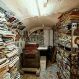 Sul pavimento invece svettano pile di libri e giornali...